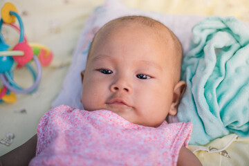 Infant Baby Girl is laying on her back in a pink bodysuit with a development toy for teething.