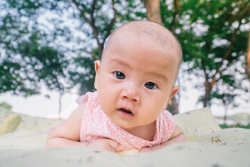 Infant Baby Girl is laying on her belly in a pink bodysuit, holding her head up.