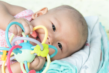 Esther Title: Infant Baby Girl is laying on her back in a pink bodysuit with a development toy for teething.