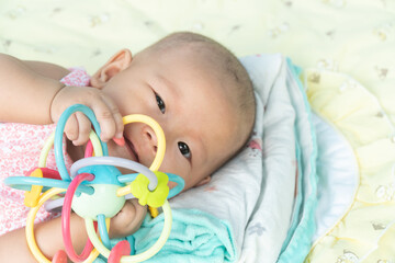 Esther Title: Infant Baby Girl is laying on her back in a pink bodysuit with a development toy for teething.