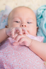 Infant Baby Girl is laying on her back in a pink bodysuit grasping her hands.