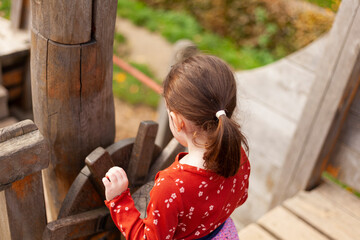 little girl in a red T-shirt plays on the playground on a pirate ship