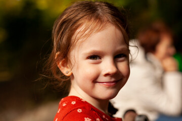 little beautiful girl in a red shirt against the background of blurred parents