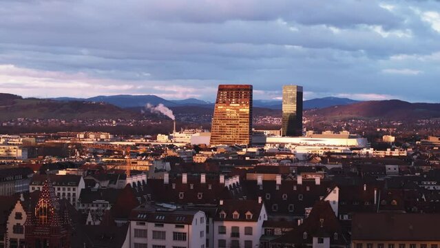 Aerial slide and pan footage of pair of high rise buildings in city at golden hour. Revealing historic houses and tower crane. Basel, Switzerland