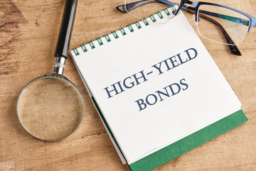 Inscription High-Yield Bonds on a notebook with a magnifying glass and glasses on a vintage...