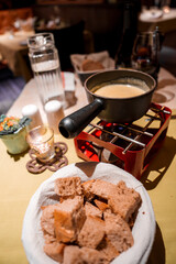Cozy dining setting with fondue meal basket of bread cubes, whole grain variety, fondue pot on red...
