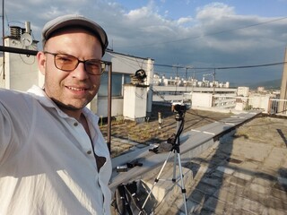 Handsome man traveler vlogger taking a selfie on a building rooftop on a sunny day in the city
