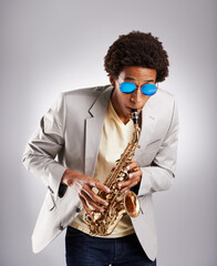 Fototapeta premium Happy, black man and music, playing the saxophone with casual suit and sunglasses in studio. African musician, jazz and instrument with confidence and trendy outfit for band with gray background