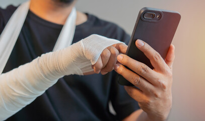 Obraz premium Man with gauze bandage or plaster cast on broken hand, broken wrist use smart phone.