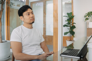 Asian man sitting and thinking, using computer laptop for work at cafe, thoughtless, have no idea, freelance concept.