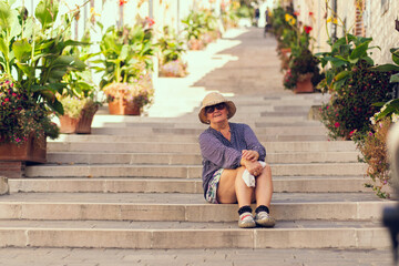 An old woman in a hat sits on the steps of a long staircase