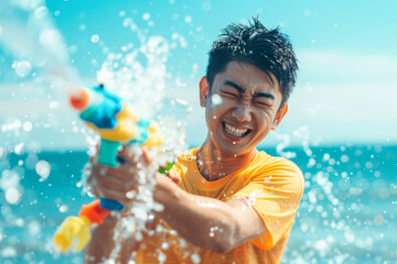 Happy traveler asian man wearing summer shirt holding colourful squirt water gun over blur sea, Water festival holiday concept