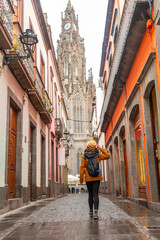 A woman wearing a yellow jacket walks down a narrow street
