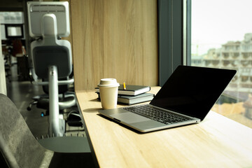 Laptop, coffee cup and notebooks on table in coworking space, close up