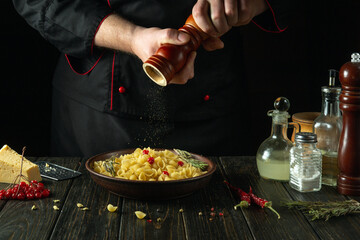 The chef adds pepper with a grinder to a bowl of pasta on the kitchen table. Low key concept of preparing a delicious lunch in a tavern