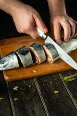 Obraz premium Slicing raw fish for salting with spices with a knife in the hands of a cook. The concept of preparing herring with fish on the kitchen table