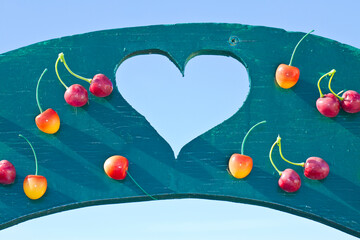 Colored wooden panel with a central heart shape and red and yellow hanging cherries - concept image