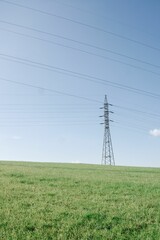 hi-voltage electric poles with cable lines at green field under clear blue sunny sky in landscape