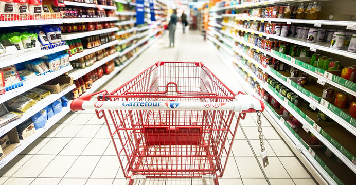 Pusty koszyk, w&oacute;zek sklepowy w supermarkecie, rozmazane tło, wnętrze sklepu, supermarketu, w&oacute;zek na zakupy, p&oacute;łki sklepowe z produktami. Hipermarket Carrefour. Warszawa, CH Arkadia. Miejsce na tekst