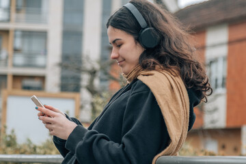 teenager girl with headphones and mobile phone on the street in winter