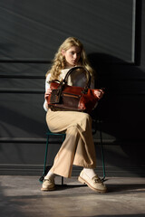 beautiful curly blond hair woman posing with a brown shopper bag near gray wall