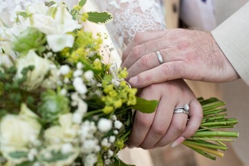 Closeup shot of the groom and bride hands with rings and a bouquet on their wedding day