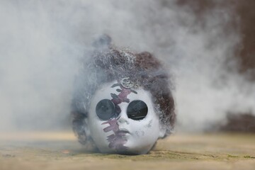 Creepy doll's head on the gorund, with buttons instead eyes, surrounded by smoke