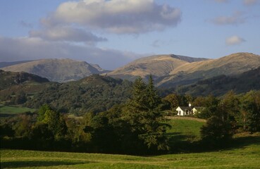 Scenic view of a cozy cottage surrounded by lush trees and evergreen mountains in Ambleside, Cumbria