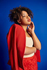 debonair stylish african american female model in vibrant outfit looking away on blue backdrop - 781174337
