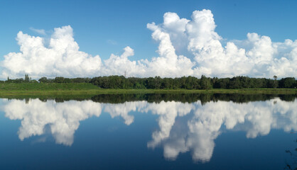 Mirror reflection of the big white clouds and green trees on the Sawgrass lake in Florida
