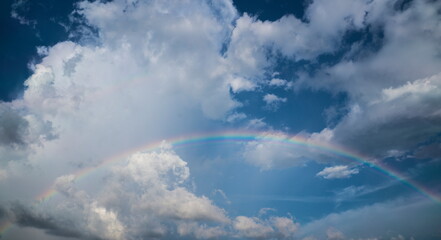 Fototapeta na wymiar Low angle shot of rainbow in blue cloudy sky