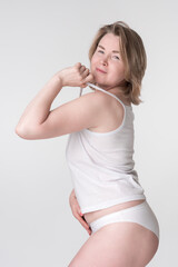 Woman wearing underwear holding strap of camisole and placing hand on stomach. Representative of concept of healthy lifestyle for women of Generation X Caucasian demographic, regardless of body type