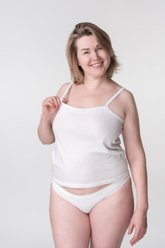Cheerful full figured middle aged woman with blonde hair, wearing white cotton camisole and panties, posing on white background. Infectious energy and positive attitude are evident from beaming smile