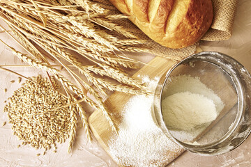 a loaf of bread,a sieve, coarse flour, grains and ears of wheat