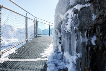 Metal walkway in snowy mountainous Murren, Switzerland. Chain link fence, icy rock face, snow on...