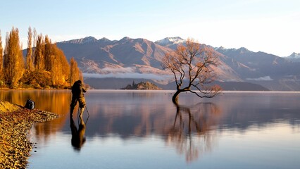 Scenic view of a person standing by the shore of a lake taking picture of the mountain in the back - Powered by Adobe