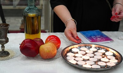 women's hands at the lighting ceremony symbolic Saturday candles with Saturday food, a collection in the form of a brochure of Saturday sindur on a wooden table covered with a white cotton tablecloth