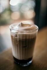 Vertical shot of a foamy coffee put on the wooden table on the blurred background