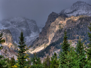 Snow-dusted Teton mountain range with lush green forest under a moody sky