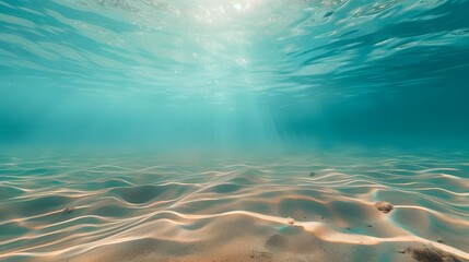 Blue tropical ocean above, seabed sand below, empty underwater background with the summer sun shining brightly, creating ripples in the calm sea water. - obrazy, fototapety, plakaty