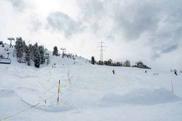Winter scene at a ski resort skiers on snow covered slope with ski lift in background. Overcast sky...