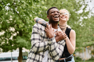 A happy multicultural couple, an African American man holding a Caucasian woman in his arms outdoors in a park.