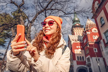 Tourist girl using map applications on her smartphone against Subotica town hall, while travelling in Serbia