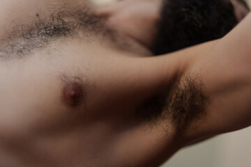 Selective focus on the body hair of a man's upper body. His beard is visible in the defocused...
