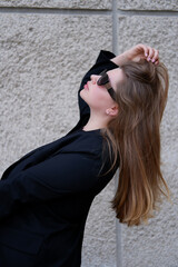 young blonde woman in a black classic jacket and black stylish sunglasses on the street. close-up portrait of a blonde woman. casual style