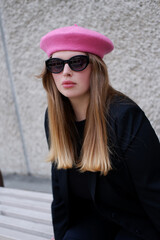 young blonde woman in a pink beret and black glasses posing for the camera. Portrait of a woman wearing a beret in Parisian style. French style. woman in sunglasses and pink beret on the street