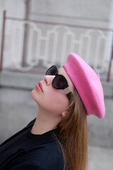 young blonde woman in a pink beret and black glasses posing for the camera. Portrait of a woman wearing a beret in Parisian style. French style. woman in sunglasses and pink beret on the street