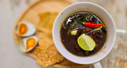 Rawon or Indonesian black beef soup, black color are from indonesian nut called kluwek. Served with lime, chili paste, salted egg, and tempe cracker. Perfect for recipe, article, or any cooking conten