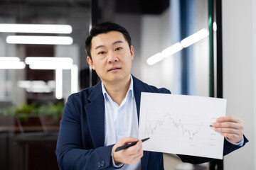 Professional Asian businessman in a suit displaying a financial report chart, engaging with the...