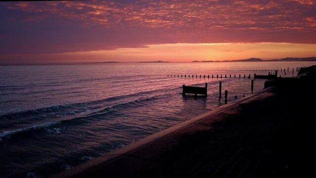 Sunset view of Bournemouth beach with a boat and wooden pier with breaking waves and orange sky
